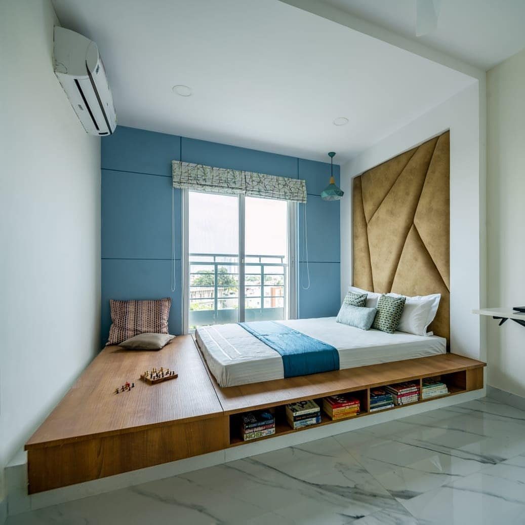 Modern small bedroom with wooden platform bed, blue wall, and gold headboard.