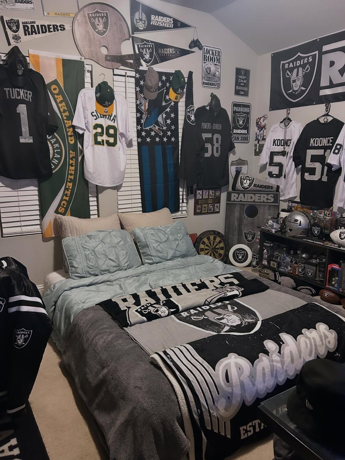 Bedroom with Raiders football jerseys and memorabilia hanging on the walls above a bed.