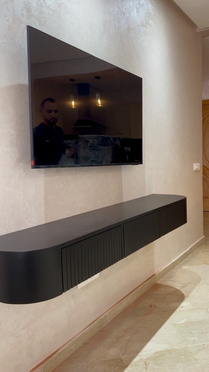 Wall-mounted television above a long black floating console on a light textured wall.