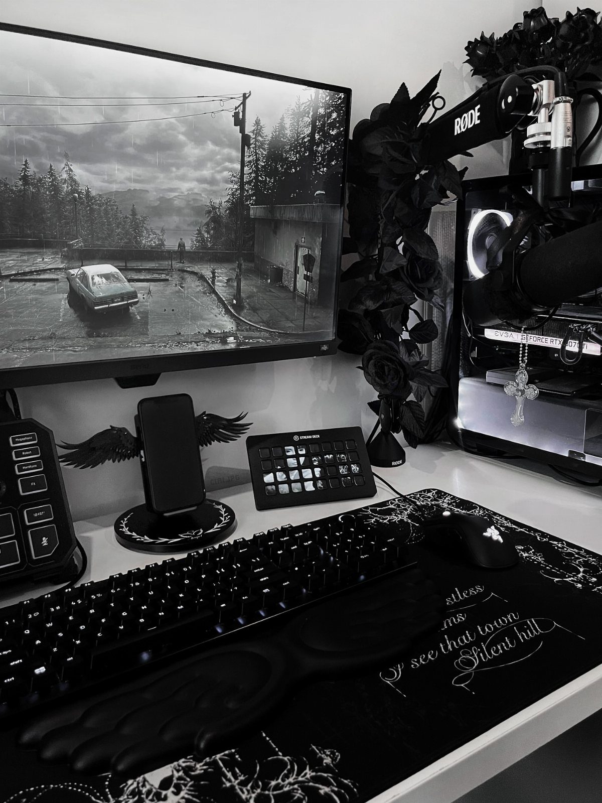 Black gaming peripherals and decorative roses on a desk with a grayscale monitor.