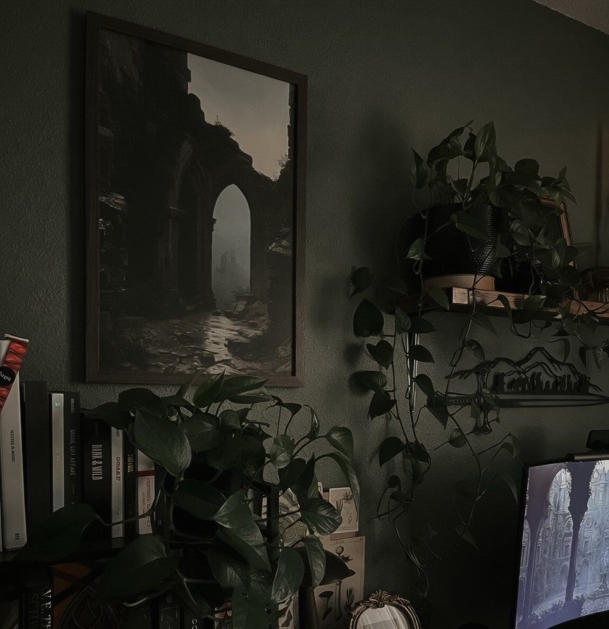 Dark green gaming nook with framed art, trailing plants, and a computer monitor.