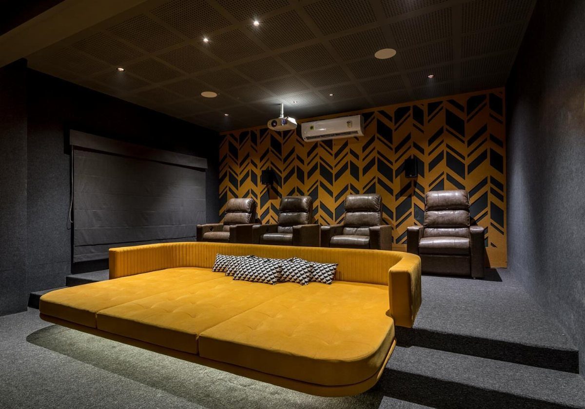 Small home cinema room with yellow daybed, leather recliners, and geometric wallpaper.