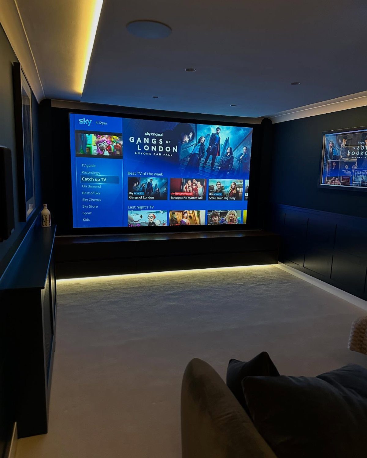 Large screen displaying a movie menu in a dark blue home cinema room.
