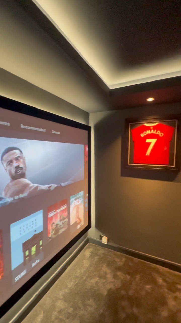 Projection screen in a small home cinema room with a framed sports jersey.