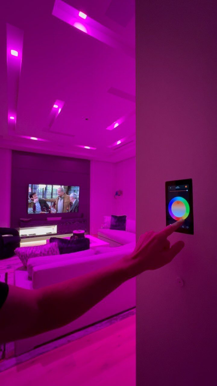 Hand touching a smart home control panel in a purple lit cinema room