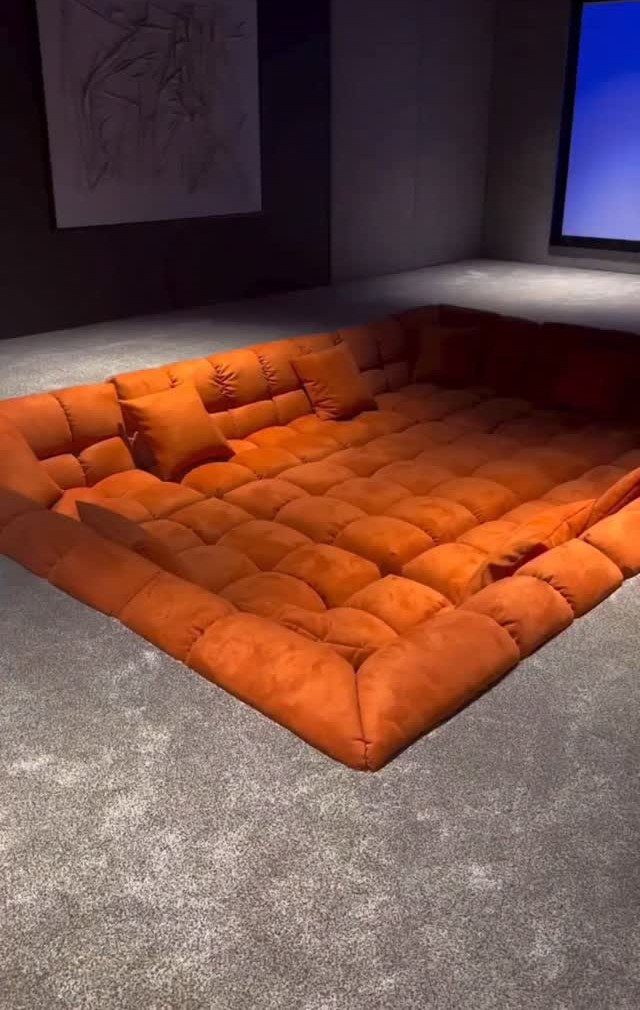 Large orange tufted floor sofa in a dark home cinema room setting