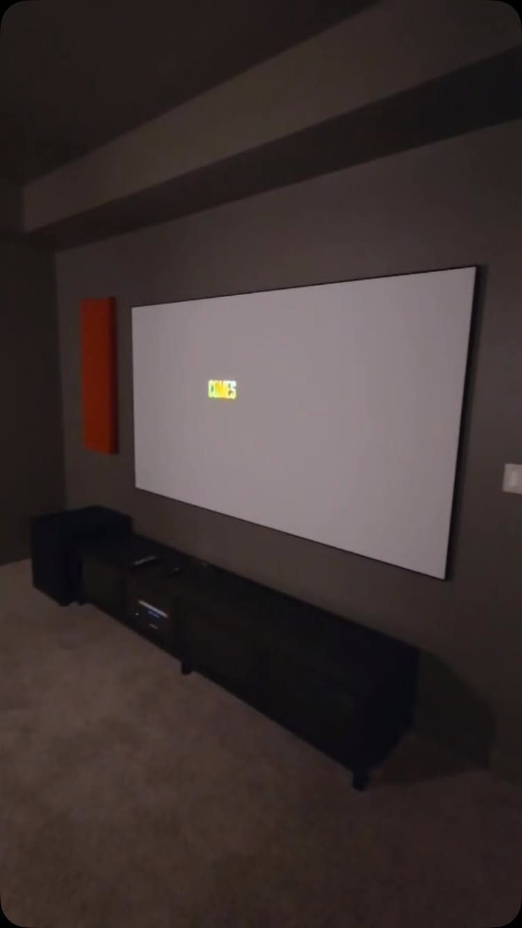 Large white projection screen on a dark grey wall with black media console