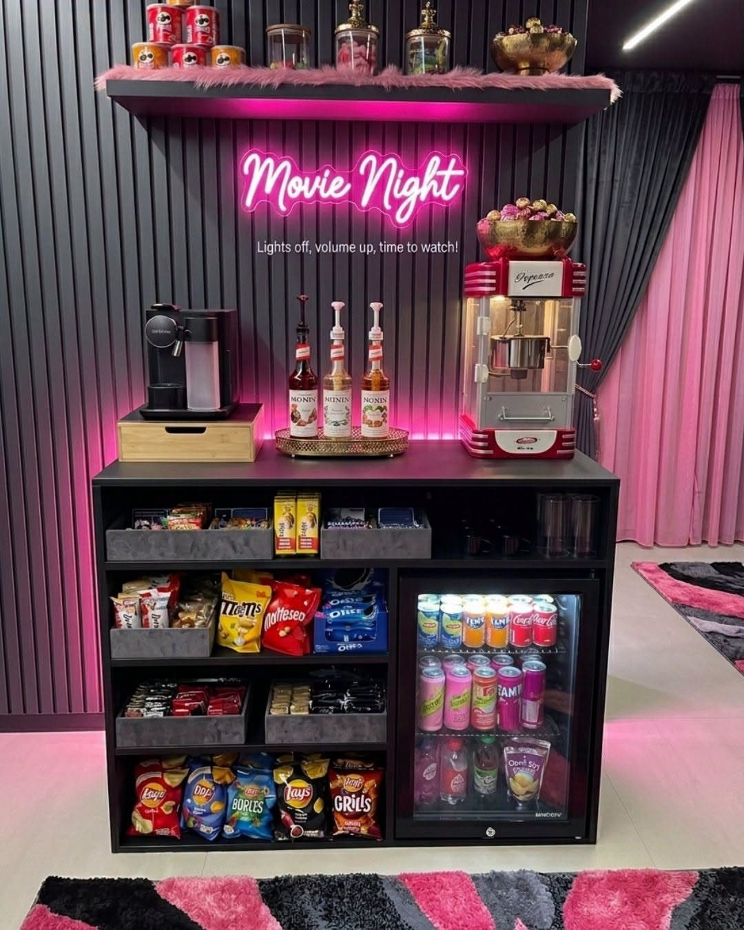 Black snack station with popcorn machine, drinks, and pink neon Movie Night sign.