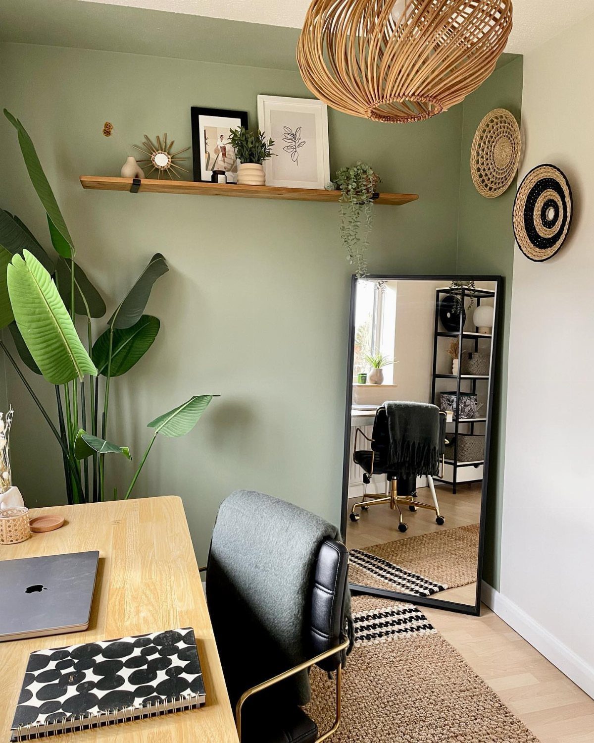 Sage green accent wall in a home office with a mirror and shelving.