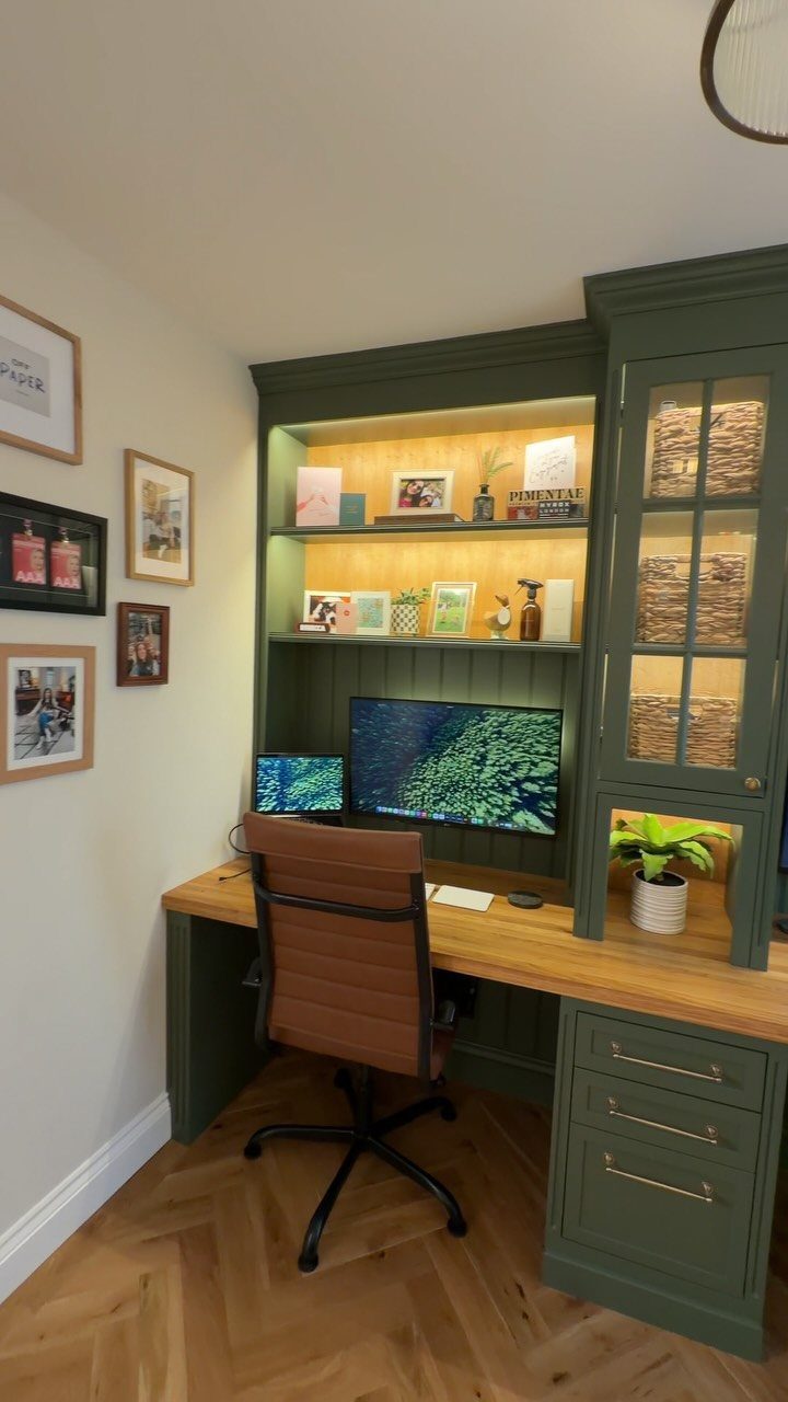 Built-in dark green home office desk with wooden top and brown leather chair.
