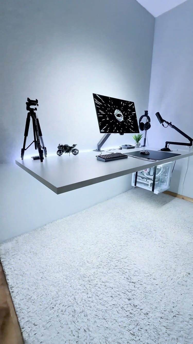 Floating white desk with computer setup and tripod in a minimalist room