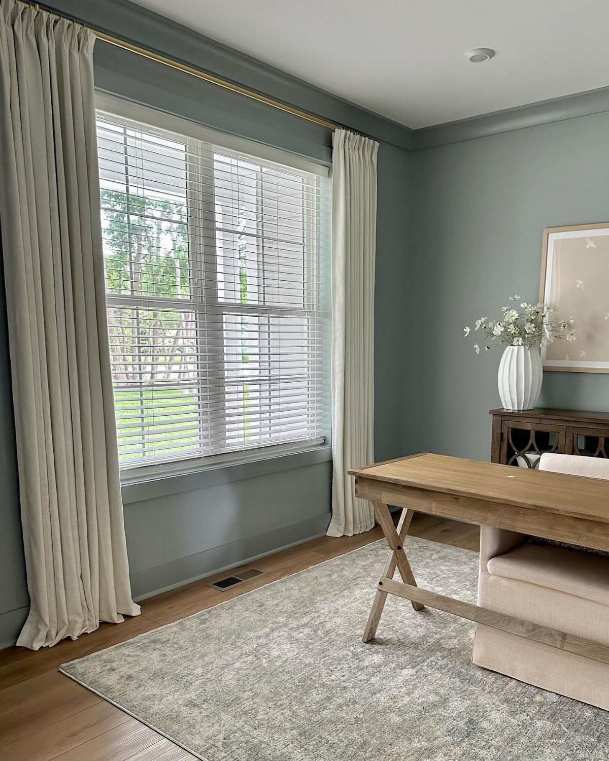 Wooden desk and grey rug in a room with blue-grey walls and curtains.