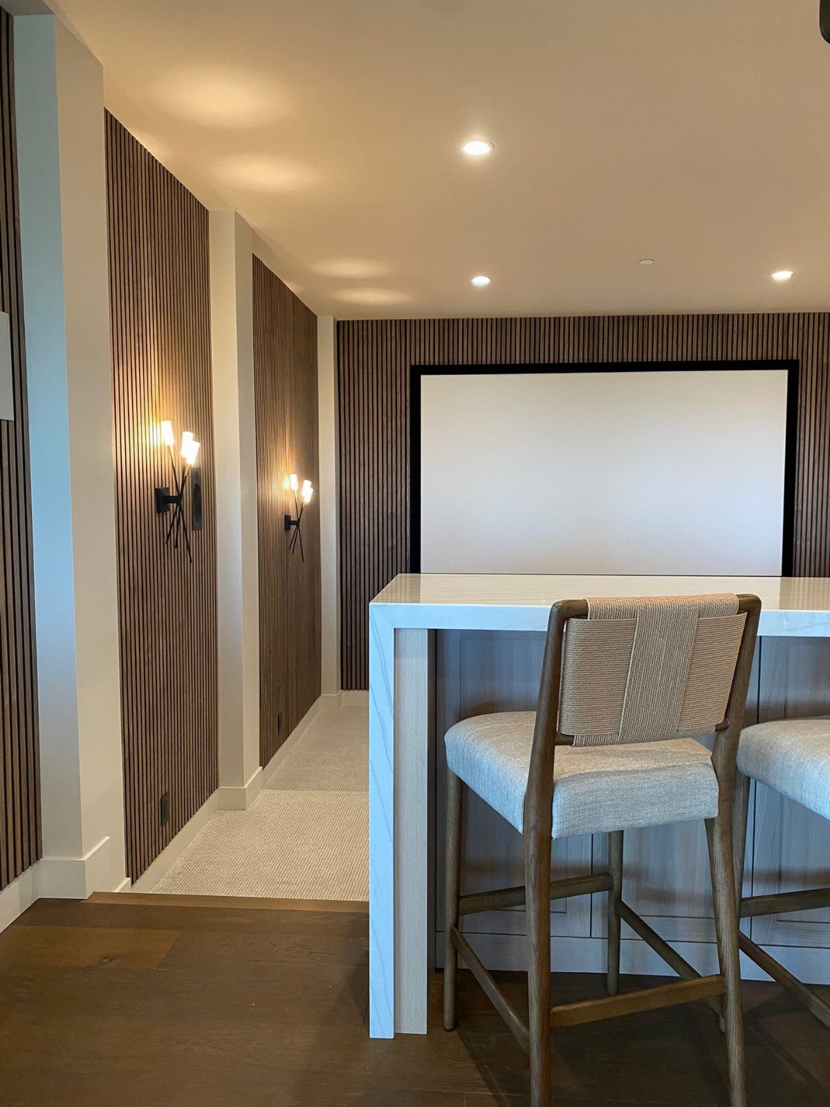 Projection screen on a slatted wall with a white bar table and stools.