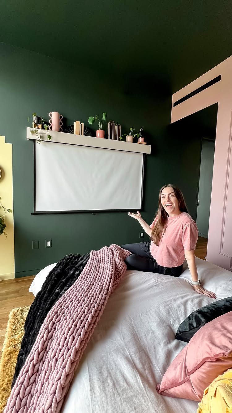 Woman sitting on a bed in a bedroom with a wall-mounted projector screen.
