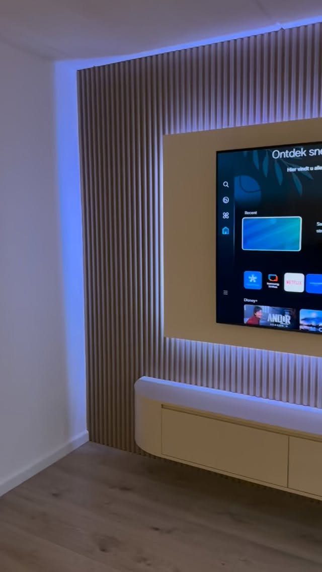 Modern home theater setup with a large TV, wooden slat wall, and blue lighting.