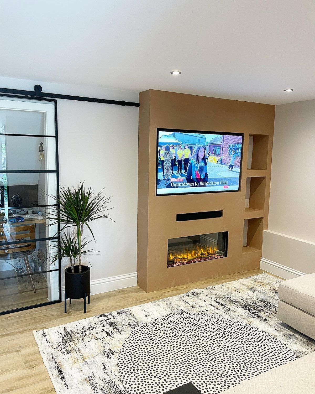 Modern media room with tan accent wall, built-in TV, and electric fireplace.