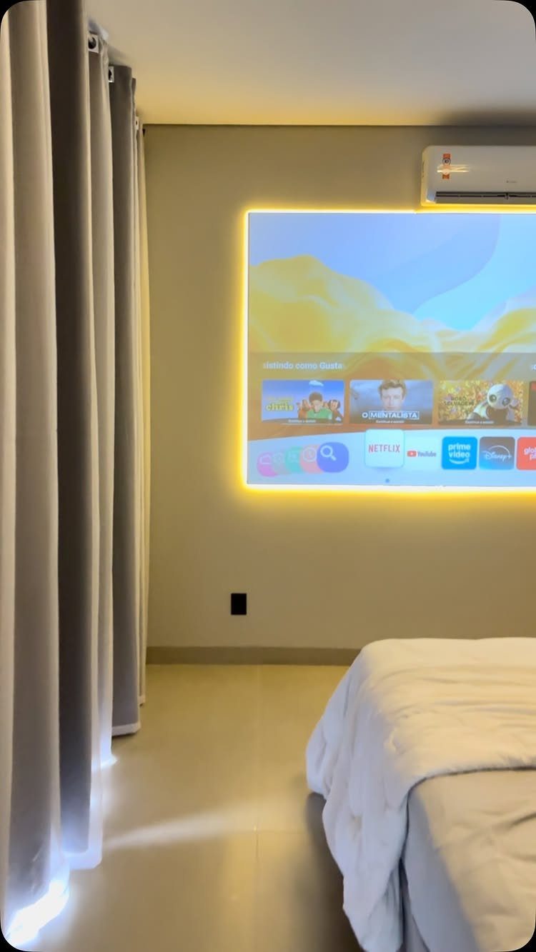 Projector screen with yellow backlight on a bedroom wall next to a bed