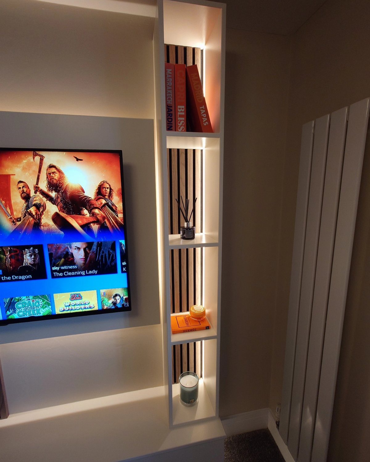 Wall-mounted television set into a white recessed unit with integrated shelving and books.