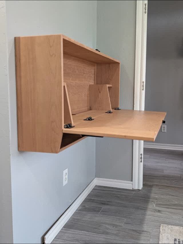 Wooden wall-mounted Murphy desk with a fold-down work surface against a grey wall.