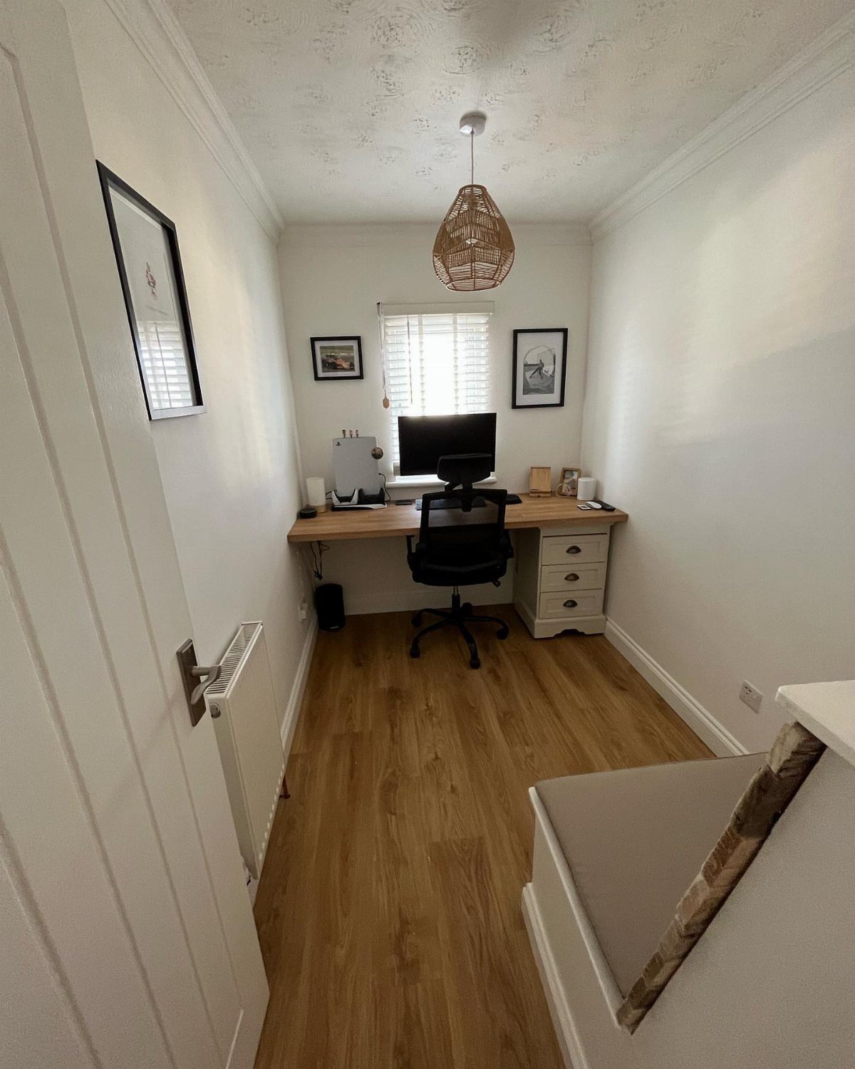 Wooden desk spanning a narrow white room with a black office chair and monitor.
