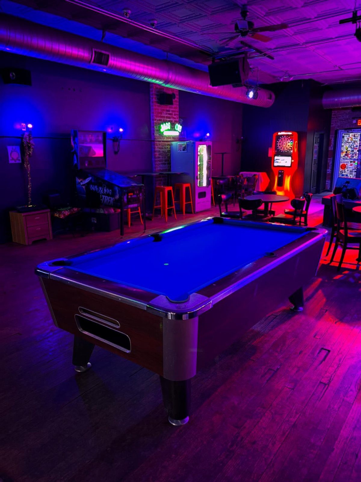 Blue felt pool table in a dark room with purple neon lighting.
