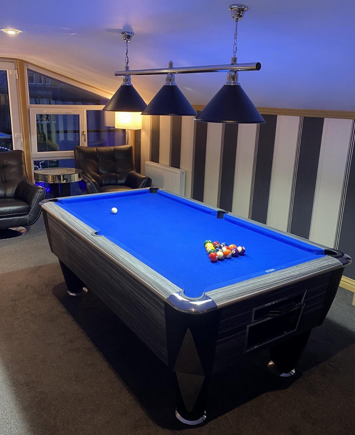 Three black cone pendant lights hanging over a blue pool table in a room.