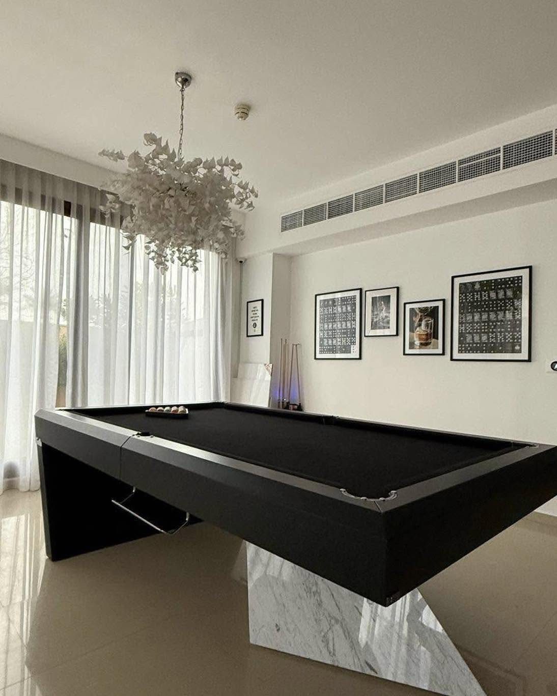 Modern black pool table with marble base in a bright, minimalist room.