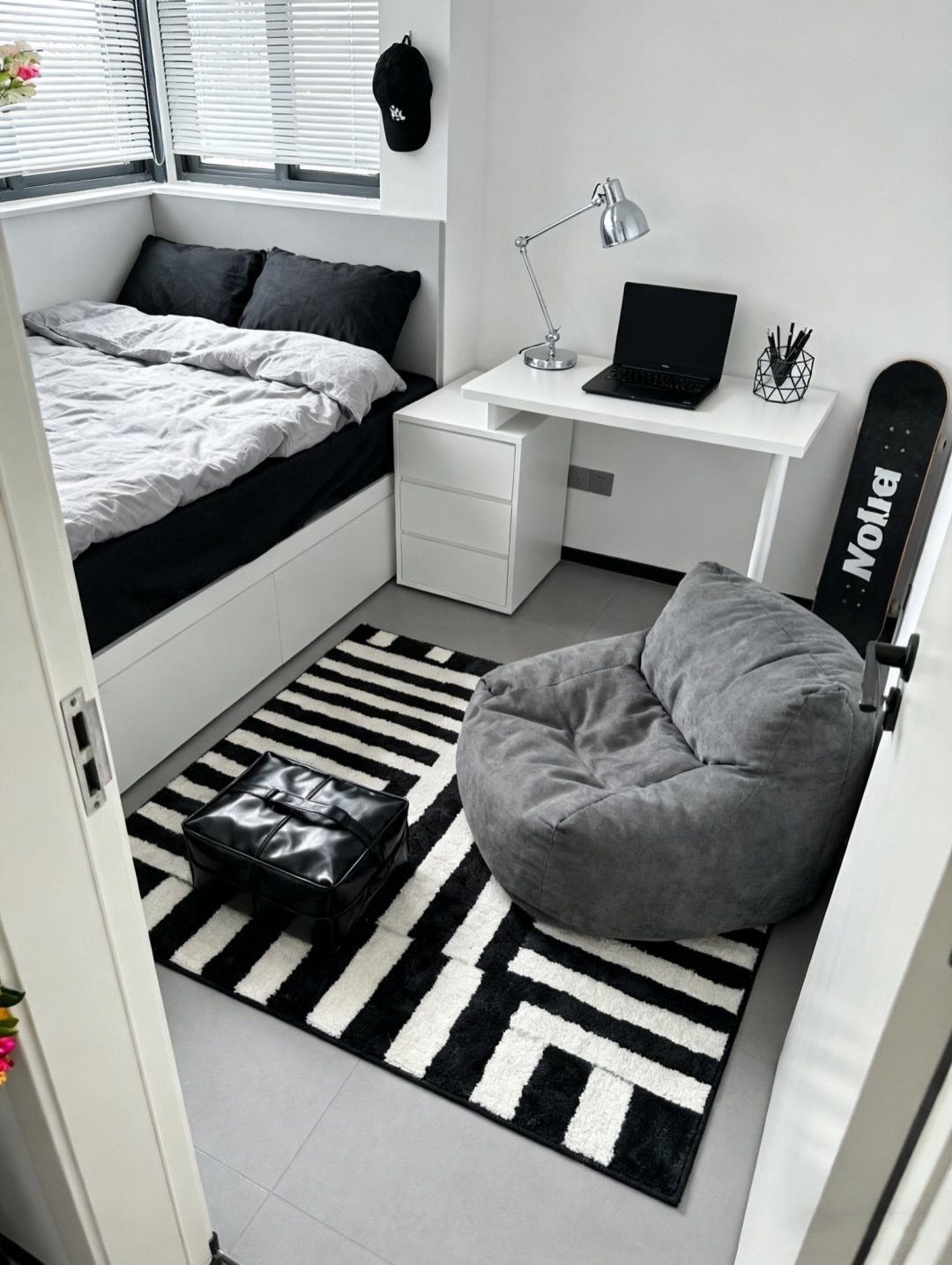 Small white bedroom featuring a compact desk, grey bean bag, and geometric rug.