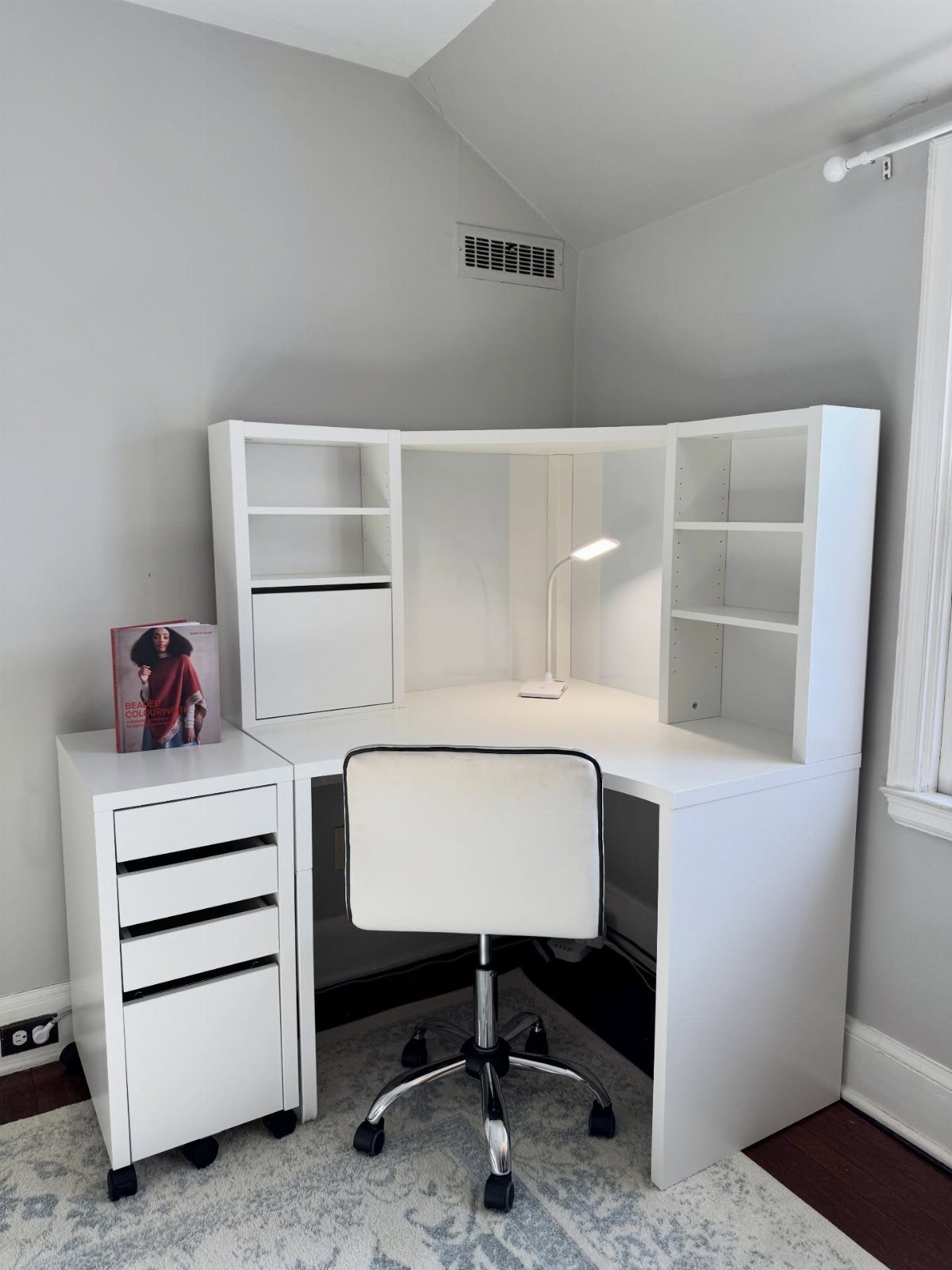 White L-shaped corner desk with shelving and a white office chair in a room.