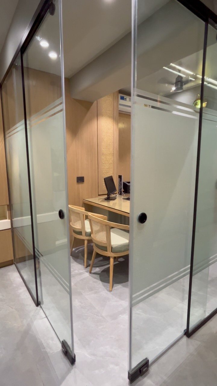 Small office with light wood desk and chairs behind frosted glass sliding doors.