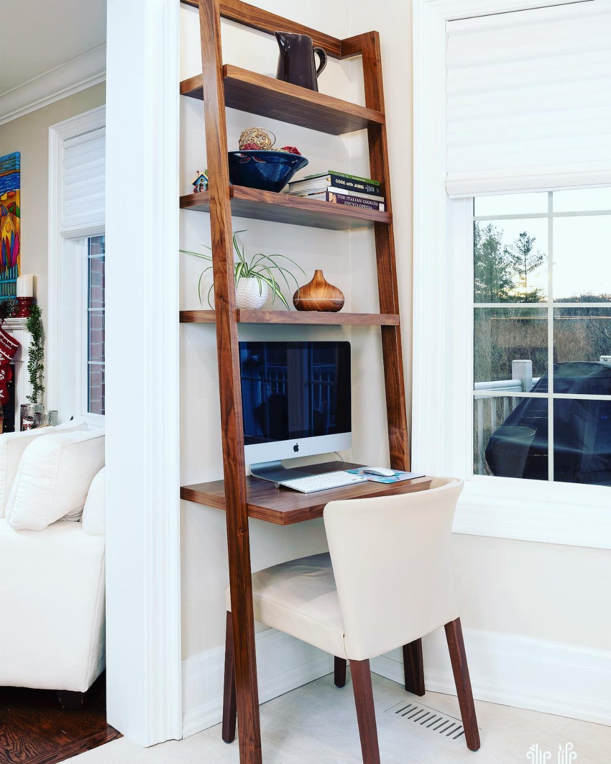 Wooden ladder desk with integrated shelving and a computer monitor in a bright room.