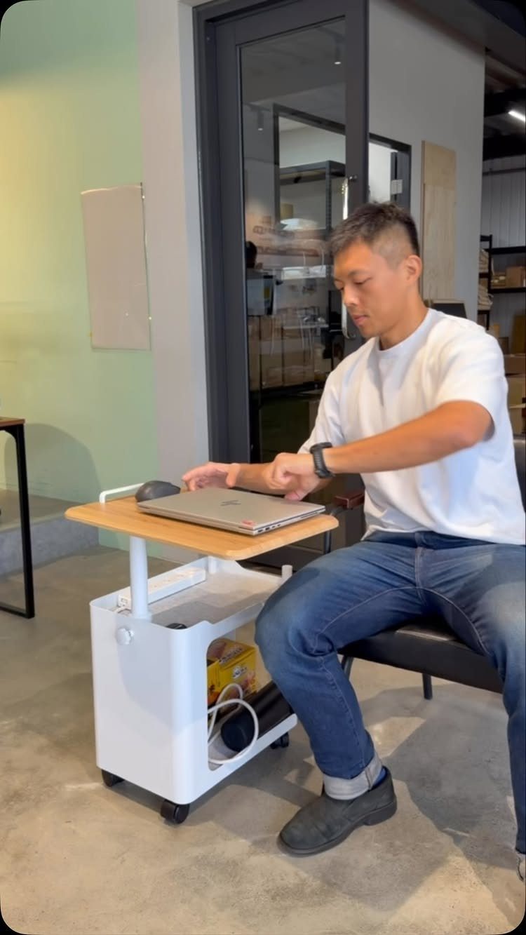 Man using a laptop on a white mobile office cart with wooden top.
