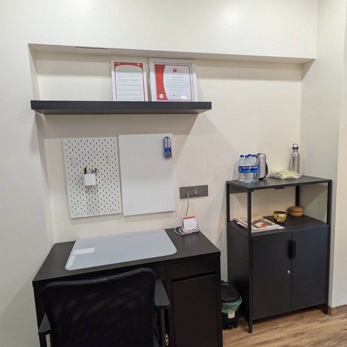 Black desk and storage cabinet in a small office with wall-mounted shelving.