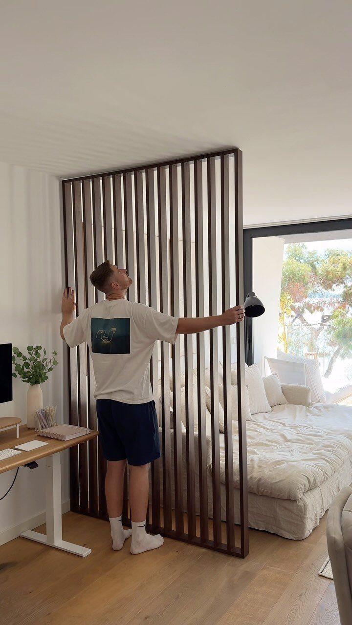 Wooden slat room divider separating a small home office desk from a bedroom
