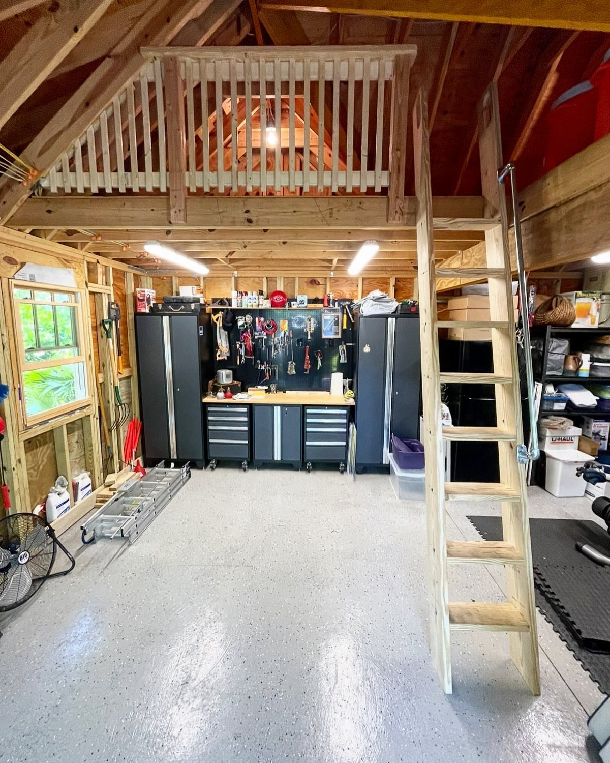 Wooden storage loft with railing and ladder inside a finished garage workshop