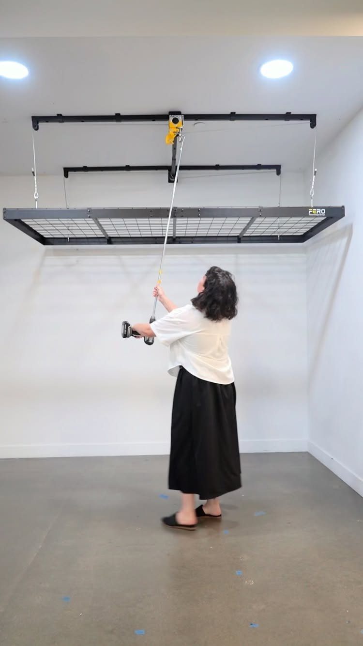 Woman lowering a black metal overhead storage rack in a white garage