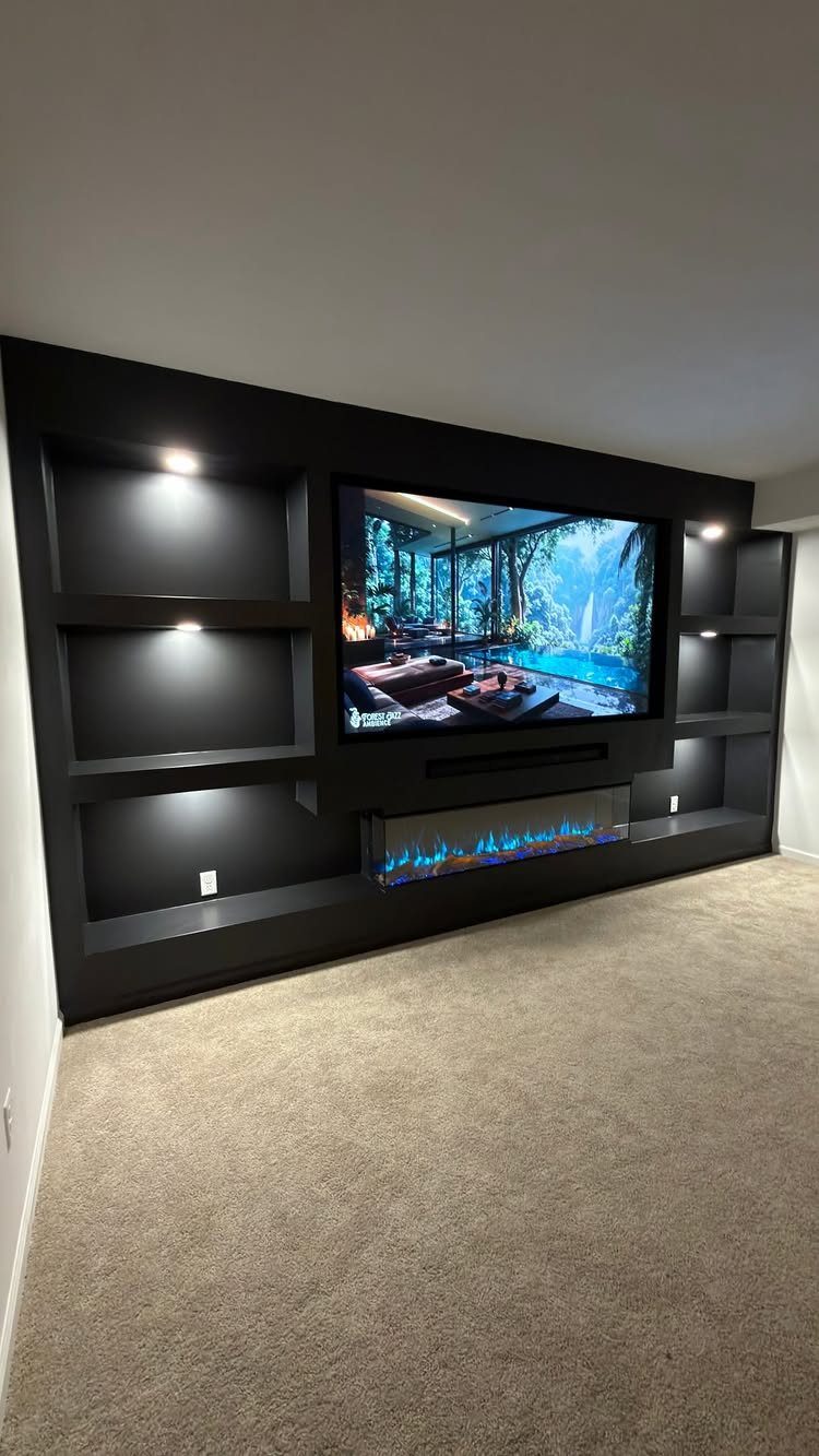 Black built-in entertainment wall with TV, electric fireplace, and illuminated side shelving.