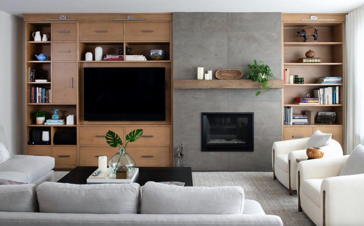 Flat-screen TV integrated into wooden built-in shelving next to a grey concrete fireplace.
