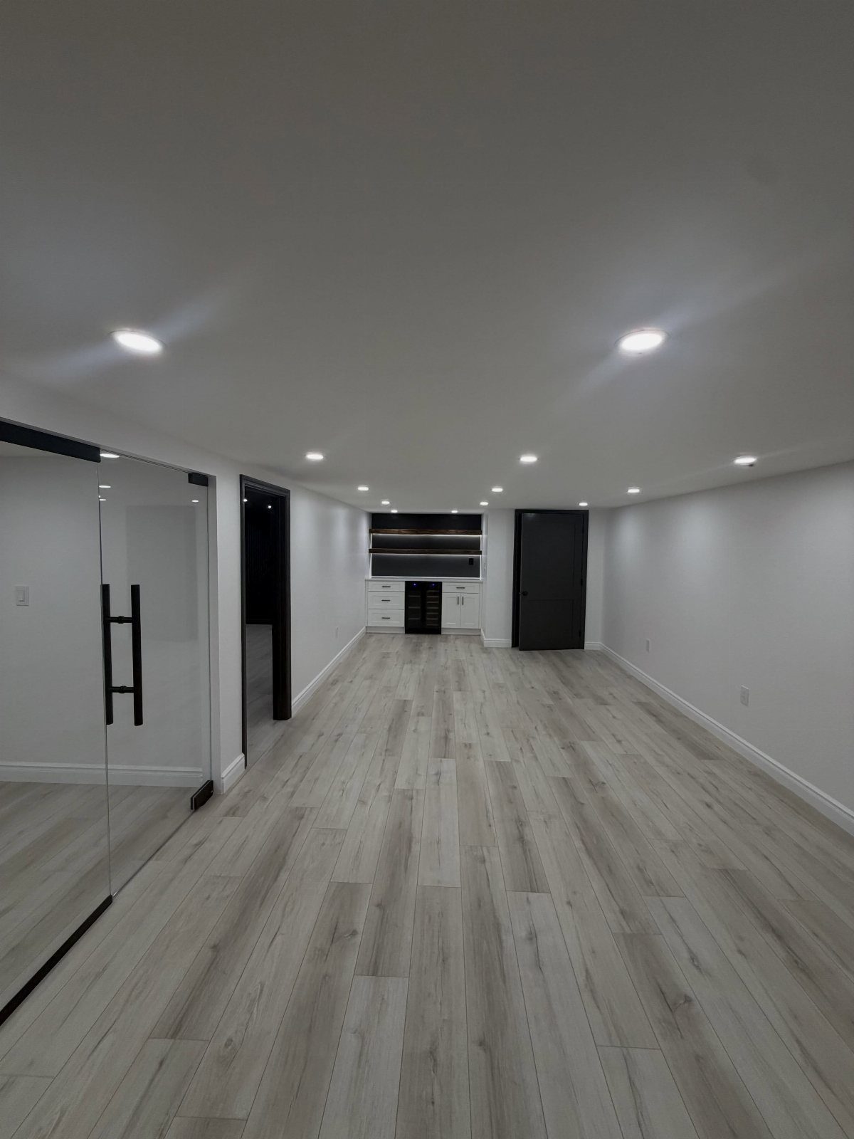 Empty finished basement with light grey flooring, white walls, and recessed lighting.