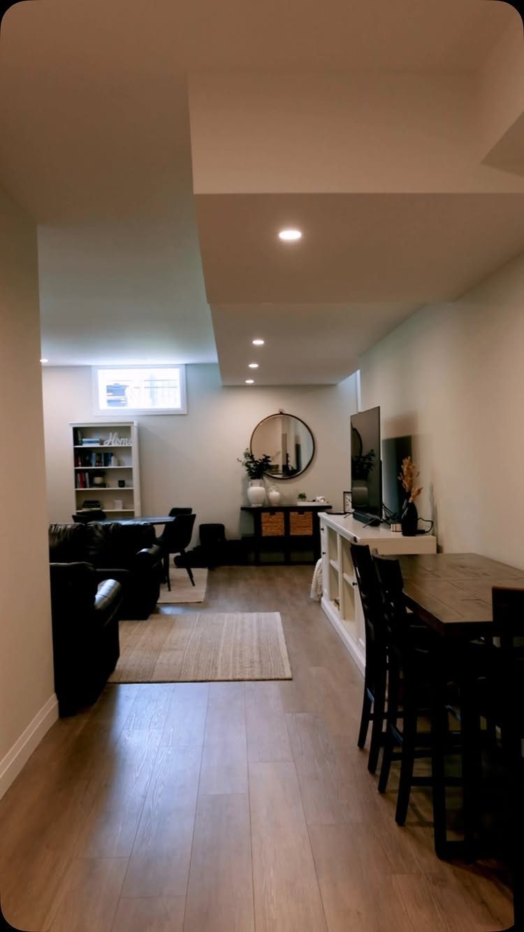 Finished basement living area with black furniture, wood floors, and neutral grey walls.