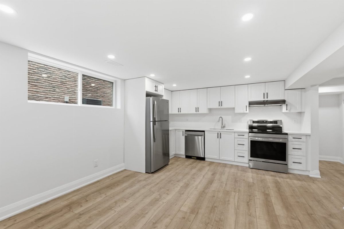 Modern basement kitchen with white cabinetry, stainless steel appliances, and light wood flooring.
