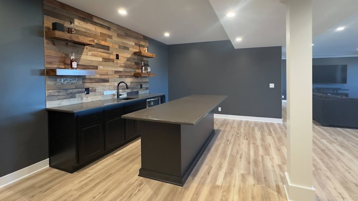 Modern basement wet bar with black cabinets and rustic wood accent wall