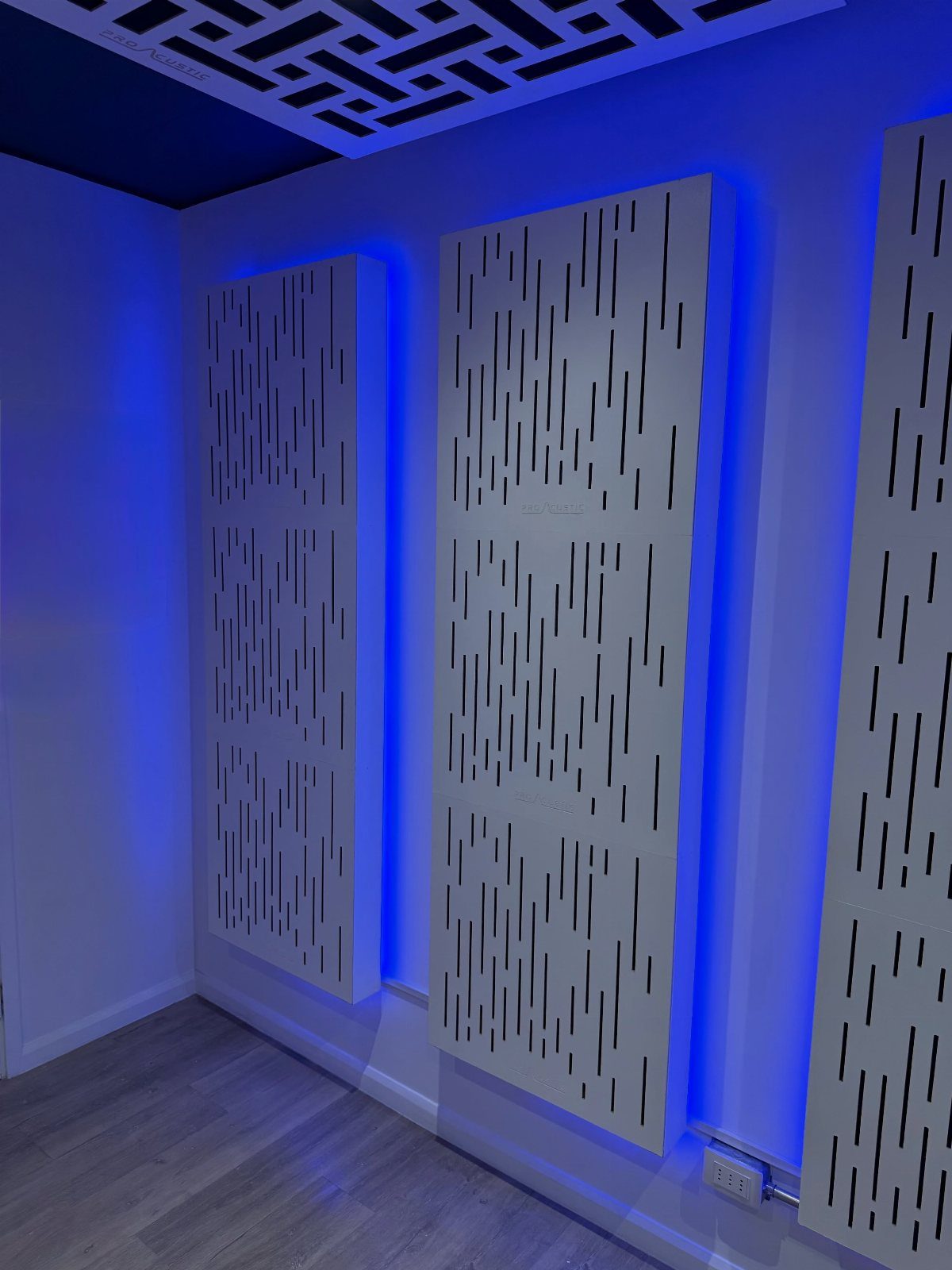 White acoustic panels with slit patterns backlit by blue LED lights on a wall