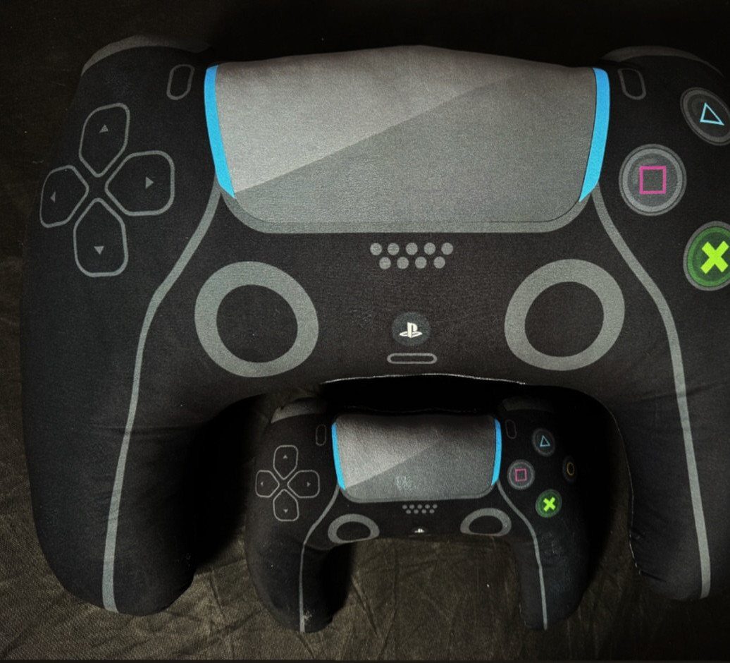Two plush throw pillows shaped like black video game controllers on leather furniture.