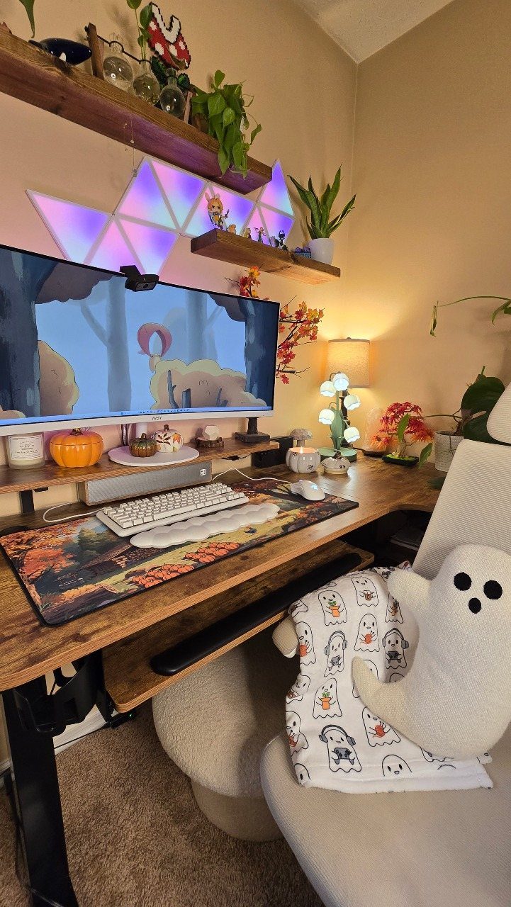 Gaming desk setup with RGB wall lights, wooden shelves, and a ghost plushie.