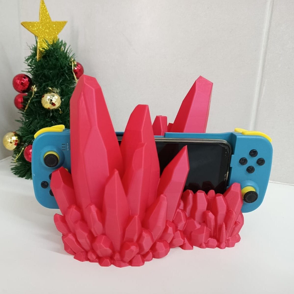 Blue Nintendo Switch held by a pink crystal-shaped stand next to a small Christmas tree
