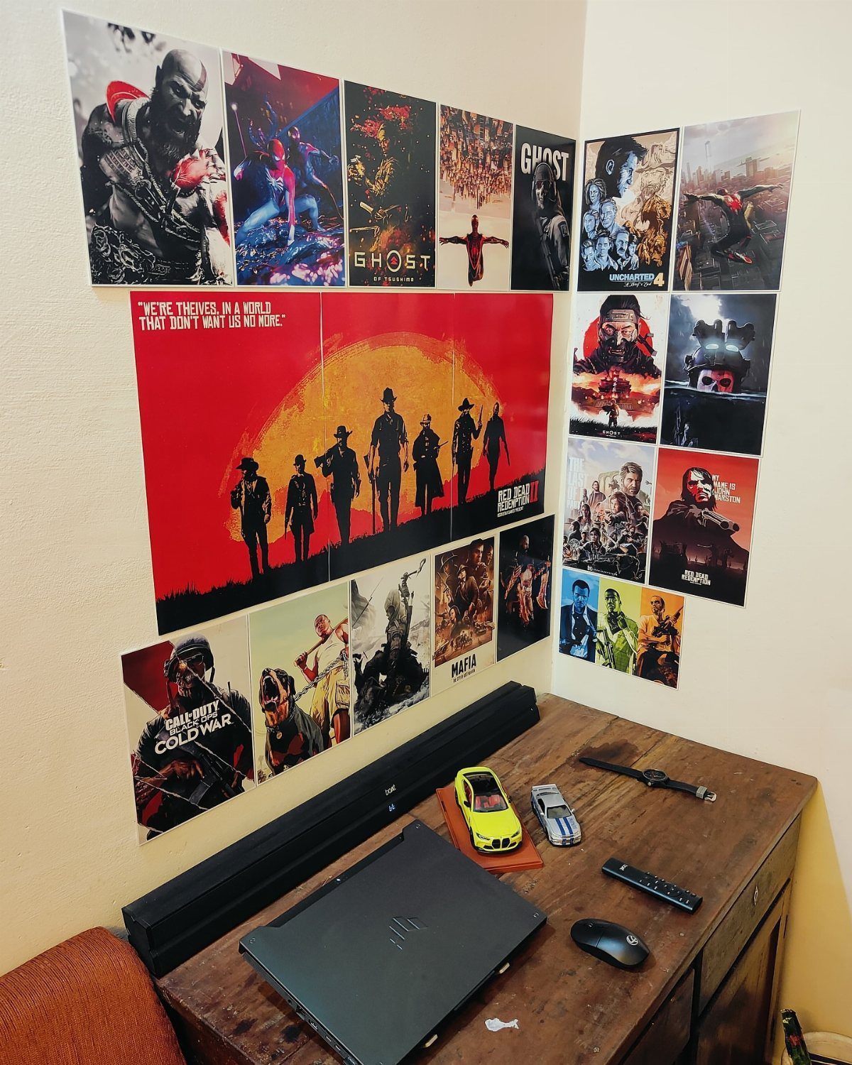 Video game posters covering a wall above a wooden desk with a laptop.