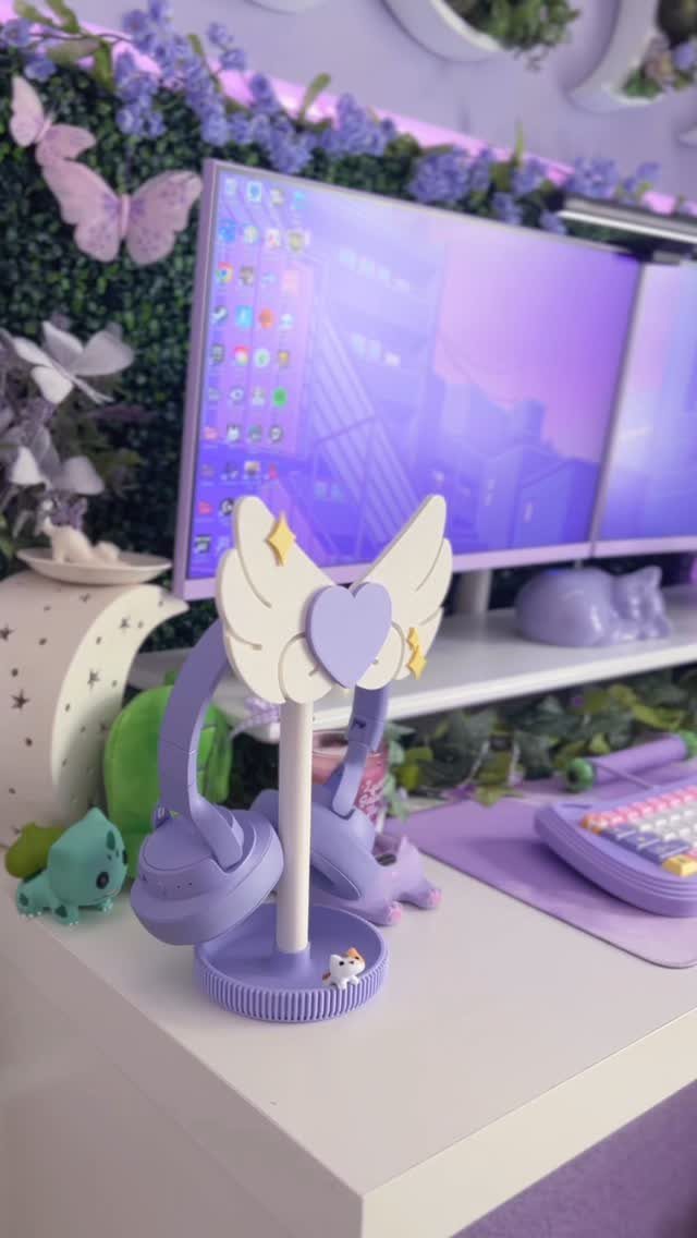 Purple headphones resting on a decorative winged headphone stand on a white desk.
