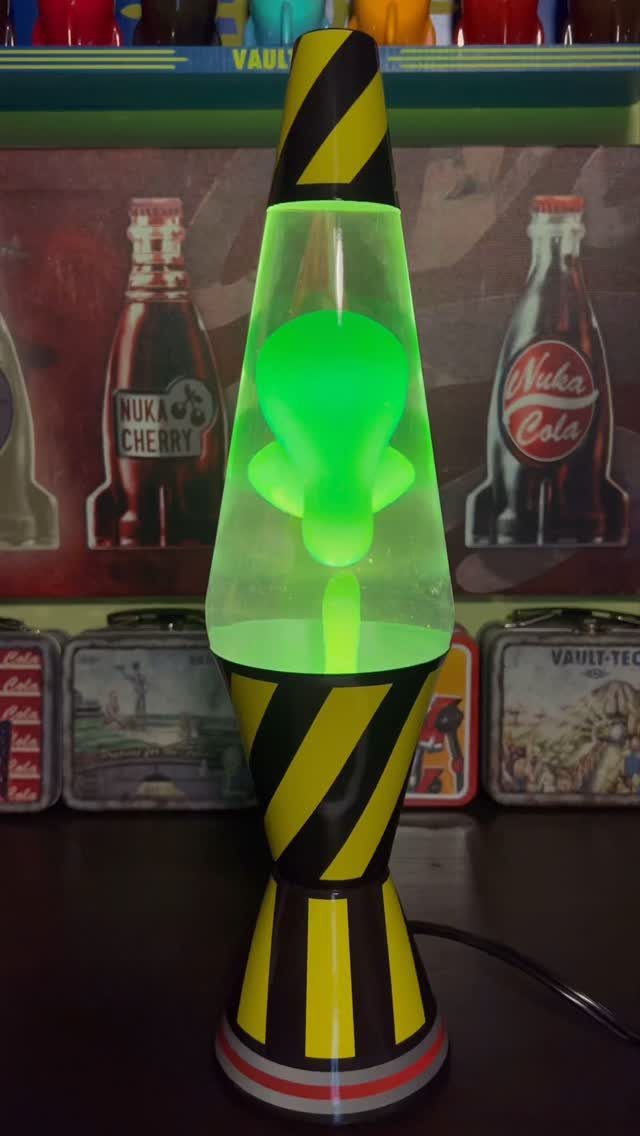 Green lava lamp with hazard stripes standing before Nuka-Cola gaming memorabilia.