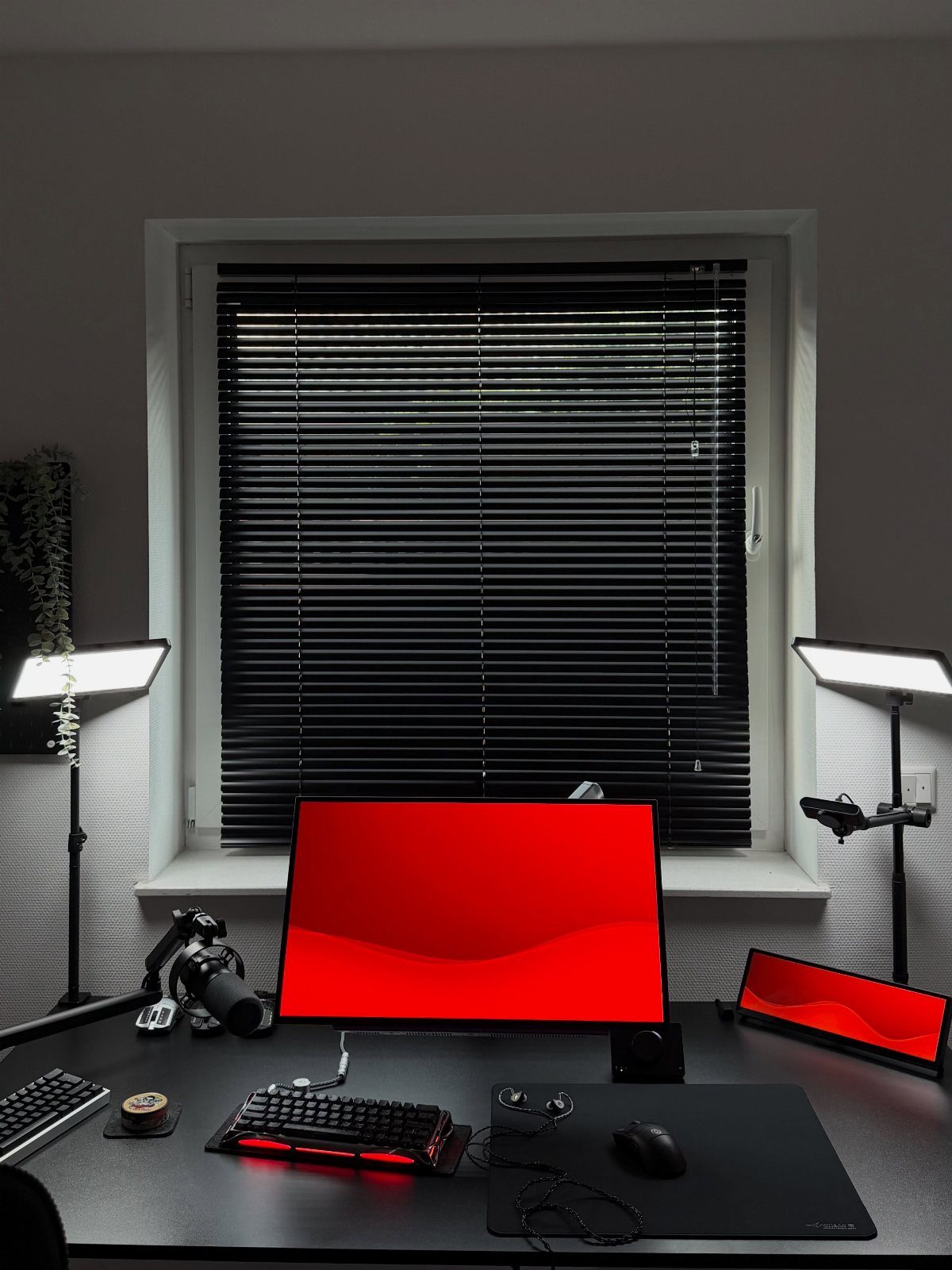 Gaming desk with red monitor, backlit keyboard, and studio lights against grey walls.
